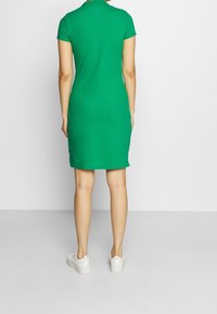 Vihreä puuvillapuseromekko lyhyillä hihoilla, istuva siluetti ja kaulus, yhdistettynä valkoisiin tennareihin. Sujuva tekstuuri, ei näkyviä kuvioita.