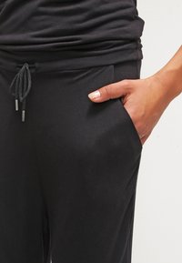 Pantalones de tela suave y negra con cintura elástica y cordón ajustable. Cuenta con bolsillos laterales y un corte relajado y ajustado.