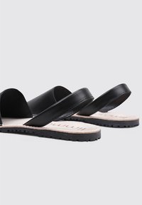 Sandalias de cuero negro con dos correas anchas y una suela de goma texturizada. Plantilla suave con marca impresa. Diseño simple y minimalista.