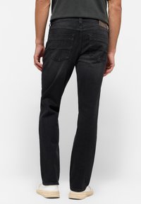 Pantalones vaqueros de denim negro con corte recto, que presentan un diseño de cinco bolsillos y costuras visibles. Combinados con zapatillas blancas.