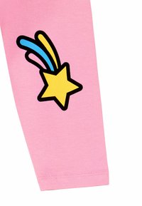 Vaaleanpunaiset puuvillaleggingsit, joissa on mustalla ääriviivalla varustettu keltainen tähti sinisiä ja keltaisia viiruja, sijoitettuna vasempaan jalkaan.