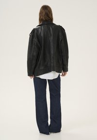 Giacca di pelle nera con una vestibilità rilassata, caratterizzata da una superficie testurizzata e spalline. Abbinata a jeans larghi in denim scuro.