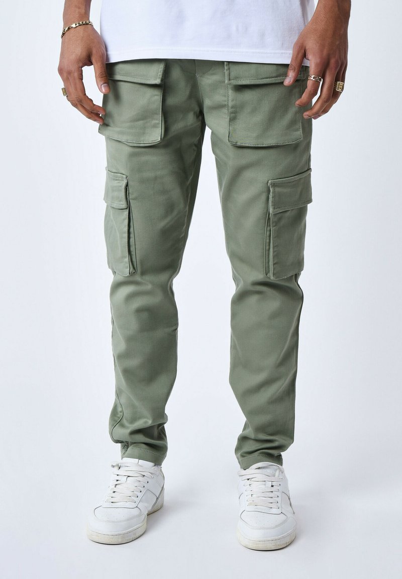 Cargobroek gemaakt van lichtgroene stof met meerdere zijzakken. Slim fit met elastische boorden en gedragen met witte sneakers.