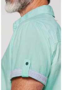 Camicetta a maniche corte di un verde menta chiaro, con dettagli a strisce sui polsini, accenti di bottoni e un design del collare rilassato. Tessuto morbido.