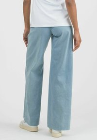 Light blue wide-leg pants made of soft fabric, featuring a relaxed fit and hemline that slightly brushes the shoes. Minimal stitching details.