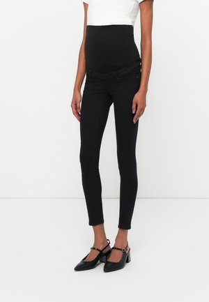 Black maternity skinny jeans with a high elastic waistband, made from denim, featuring a front zipper and sleek design. Paired with black slingback heels.