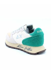 Weiße Sneaker mit grünen und beigen Akzenten, ausgestattet mit einem strukturierten Design, einem gezahnten Mudguard und dem Aufdruck "Schneller laufen" auf der Sohle.