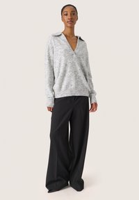 Lysegrå v-hals sweater med krave-design og ribbede manchetter, parret med sorte, vidde ben bukser. Glat tekstur, minimal mønster.