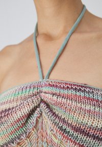 Πλεκτό κοντομάνικο τοπ με πολύχρωμο σχέδιο σε τόνους πράσινου, ροζ και μωβ. Διαθέτει ελαφριά μπλε strap που δένει στο λαιμό.