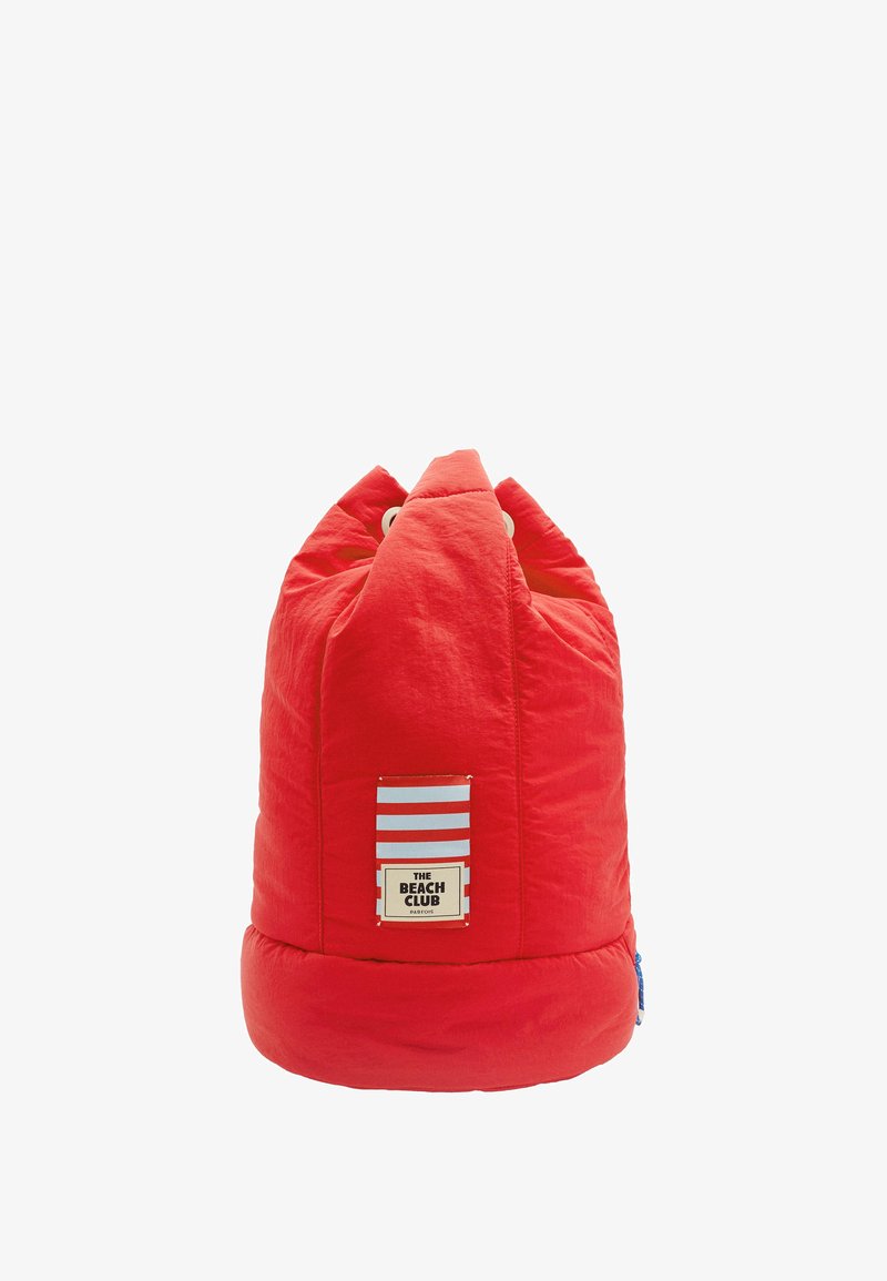 Czerwony, pikowany worek z fasolą z zaokrągloną podstawą, dwoma szczytami i naszywką z logo przedstawiającą niebieskie i białe paski. Teksturowana tkanina z widocznymi szwami.