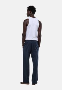 Un débardeur blanc sans manches et un pantalon de lounge bleu foncé à taille élastique. L'individu est vu de dos, pieds nus. Design simple, coupe décontractée.