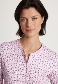 Rosa blumengemusterte Kleidung mit rundem Kragen und Knopfverschluss, ausgestattet mit einer weichen Stofftextur und kleinen navyblauen und weißen Blütenmotiven.