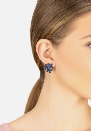 Blue floral cluster stud earring worn on the left ear of a woman with light brown hair pulled back.