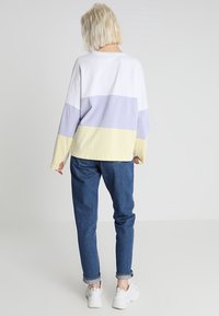 Sweter w blokach kolorystycznych w białym, lawendowym i jasnokremowym kolorze o luźnym kroju, w zestawieniu z podwiniętymi niebieskimi dżinsami i białymi trampkami.