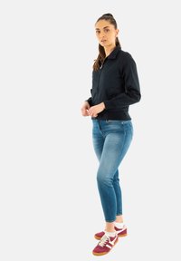 Zwarte bomberjack met een kraag, twee voorzakken, gecombineerd met slim-fit blauwe jeans en bordeauxrode sneakers met witte accenten en crèmekleurige veters.