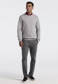 Lichtgrijze trui met een bordeauxrode kraag, gecombineerd met donkergrijze broek en zwarte sneakers. Eenvoudig ontwerp met elastische manchetten en tailleband.