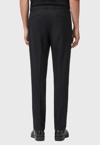Pantaloni neri con una vestibilità su misura, design con frontale piatto, due tasche posteriori e passanti per cintura, realizzati in tessuto testurizzato, indossati con scarpe nere.