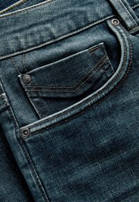 Poche de jean en denim bleu foncé avec des coutures visibles, des rivets et une petite poche pour pièces à l'intérieur de la poche avant principale.