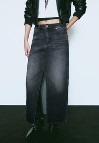 Jupe en denim foncé avec une fente frontale, coupe décontractée et design à cinq poches. Fini avec des coutures visibles et une fermeture à bouton.