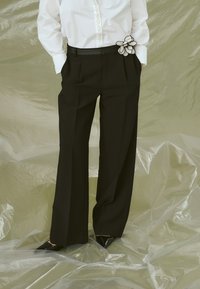 Black wide-leg trousers with side pockets and a smooth texture. Accented with a white floral detail on the waistband. Paired with a white shirt.