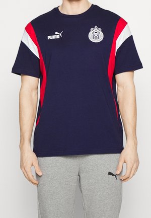 T-shirt bleu marine à manches courtes avec des rayures d'accent rouge et blanc, arborant un logo Puma sur la poitrine gauche et un blason en haut à droite.