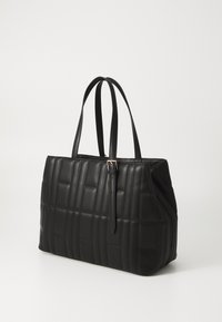 Sort quiltet tote taske med glat læder, to robuste håndtag, rektangulær form og hardware i gulltonet accent. Subtil tekstur detalje over det hele.