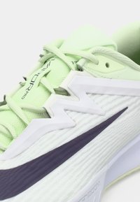 Αθλητικό παπούτσι σε ανοιχτό πράσινο χρώμα με υφή στην επάνω πλευρά, λευκές λεπτομέρειες, μωβ ρίγα και μοναδικό κυματιστό σχέδιο στην περιοχή των κορδονιών και στην πλευρά.