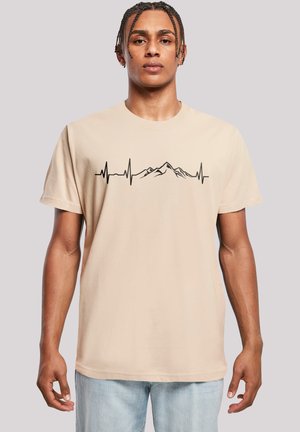 Beige cotton T-shirt featuring a black heartbeat line and mountain silhouette design across the chest. Short sleeves and crew neckline.