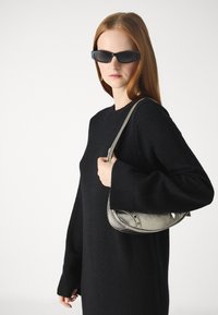 Melna adīta džemperis ar garām piedurknēm, kopā ar metālisku sudraba rokas somu ar izliekumu un delikātu tekstūru.