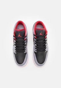 Schwarze und graue Sportschuhe mit roten Akzenten, ausgestattet mit einem glatten Leder-Obermaterial, perforierter Zehenpartie und schwarzen Schnürsenkeln. Ikonisches Logo auf der Zunge.