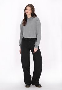 Felpa grigia corta con collo a cappuccio, abbinata a jeans neri a gamba larga e alta vita. Texture morbide e vestibilità rilassata per entrambi gli articoli.