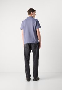 Polo bleu avec un col, à manches courtes et une texture lisse, associé à un jean gris foncé et des chaussures noires.