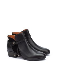 Botines de cuero negro con punta afilada, tacón bajo, cortes laterales y detalle decorativo de cordones. Interior forrado con cuero marrón.
