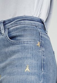 Lichtblauwe denim jeans met een aansluitende taille, voorzien van kleine gouden bijenborduursels op de voorzak. Rekbaar materiaal, gladde textuur.