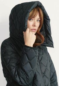 Czarna pikowana kurtka puchowa z dużym kapturem, o błyszczącej fakturze i diamentowym wzorze. Widoczny zamek błyskawiczny i elastyczne mankiety.