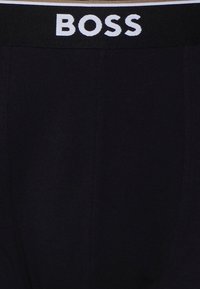 Črne bombažne bokserice z črnim elastičnim pasom, na katerem je bel napis "BOSS". Gladka tekstura, prilegajoč oblik.