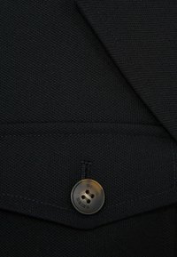 Materialul pentru sacoul negru are o țesătură texturată, cu un buton rotund maro, inscripționat cu "REISS". Include detalii cusute și un buzunar cu clapă.