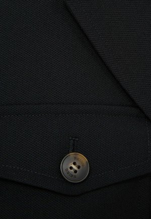 Černý blazerový materiál s texturovanou vazbou, s kulatým hnědým knoflíkem s vyrytým nápisem "REISS". Obsahuje prošívané detaily a klopu kapsy.