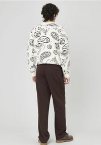 Pull blanc avec des motifs paisley et floraux noirs, associé à un pantalon marron foncé. Texture en maille douce et coupe décontractée. Chaussures à lacets marron.