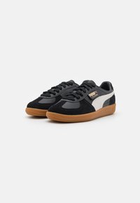 Sneakers in suede e pelle neri con una striscia laterale grigia chiara e suola in gomma marrone. Presentano lacci rotondi e linguetta imbottita.