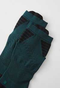 Teal ja mustad kootud kompressiosokid, millel on tekstureeritud mustrid ja soonilised äärised täiendava haarde ja toe tagamiseks.