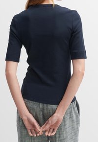 Marineblå ribbet t-shirt med korte ærmer, rund halsudskæring og tætsiddende pasform. Bæres med teksturerede, lyse bukser.