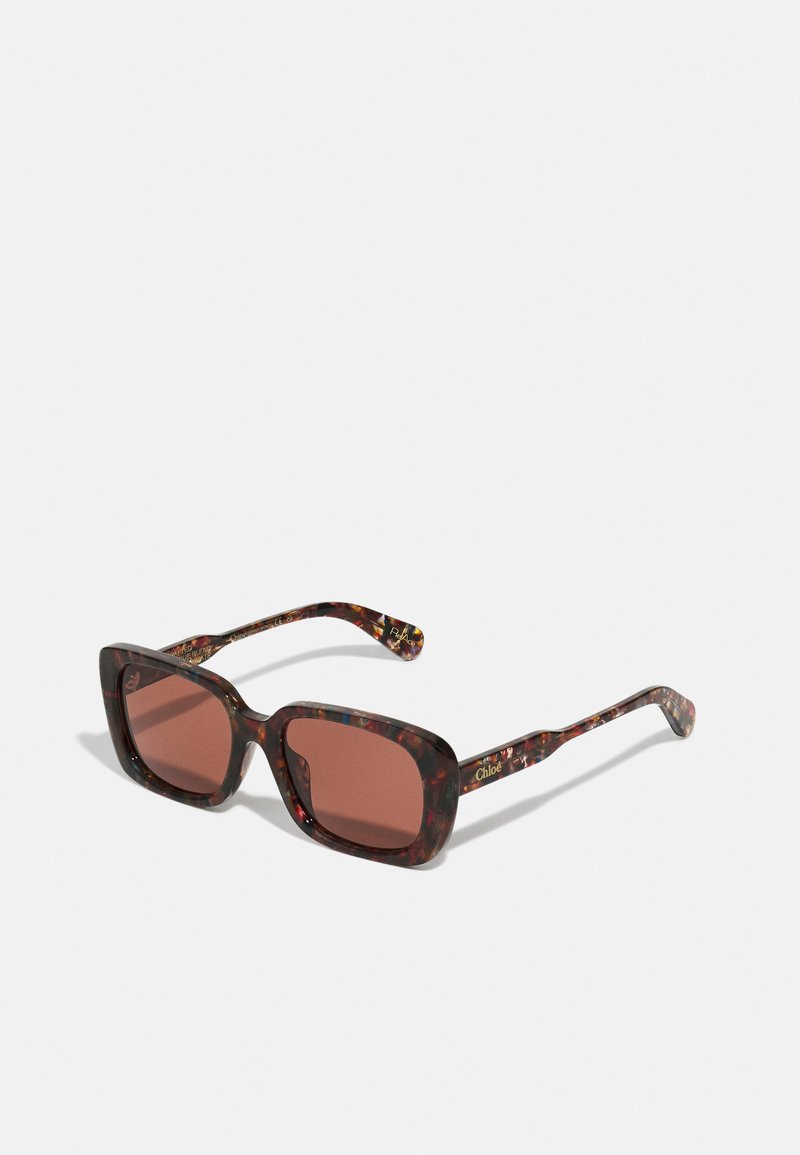 Occhiali da sole a tartaruga con montatura squadrata e lenti colorate di marrone. Presentano dettagli dorati e motivi decorativi sulle asticelle.