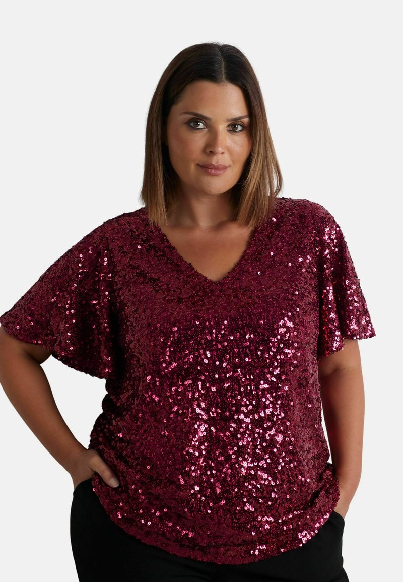 Top bordeaux con paillettes, scollo a V e maniche corte, caratterizzato da una vestibilità ampia e una texture lucida, abbinato a pantaloni neri.