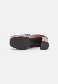 Chaussure à plateforme en cuir verni de couleur brun-rouge avec un talon épais. Elle présente une surface lisse et brillante ainsi qu'une semelle extérieure en caoutchouc noir.