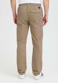 Light brown, textured pants with an elastic waistband, featuring a single back pocket and a logo tag, paired with white sneakers.