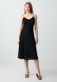 Robe en tricot noir avec un corsage ajusté et une jupe évasée. Dotée de fines bretelles spaghetti et d'un motif géométrique texturé sur l'ensemble.