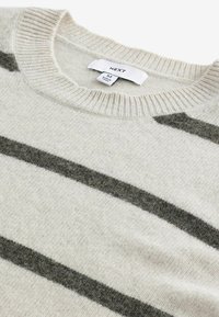Cream-colored sweater with dark gray stripes, knitted texture, ribbed neckline, and label reads "NEXT," size medium.