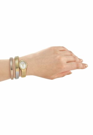 Poignet féminin portant une montre en or avec lunette en diamants et deux bracelets métalliques extensibles aux tons rose et argenté.