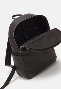 Sac à dos en cuir noir texturé avec un intérieur spacieux, une poche avant zippée et des bretelles réglables. La doublure est en tissu noir.